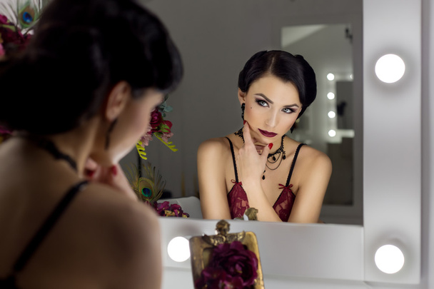 beautiful sexy young woman flaunts front of the mirror in the dressing room in lacy underwear in a retro style with bright make-up and beautiful evening hairstyles , shot in the style of the 20s - Foto, imagen
