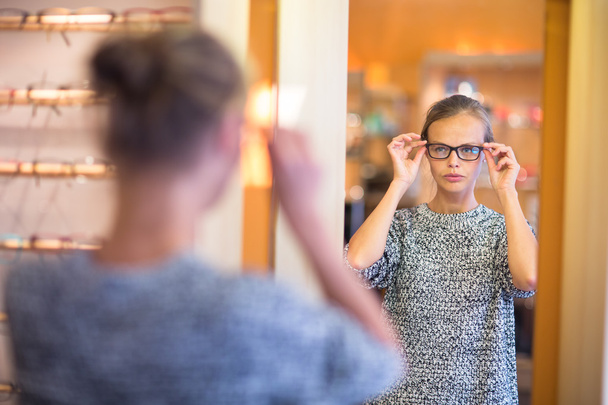Pretty, young woman choosing new glasses frames - 写真・画像