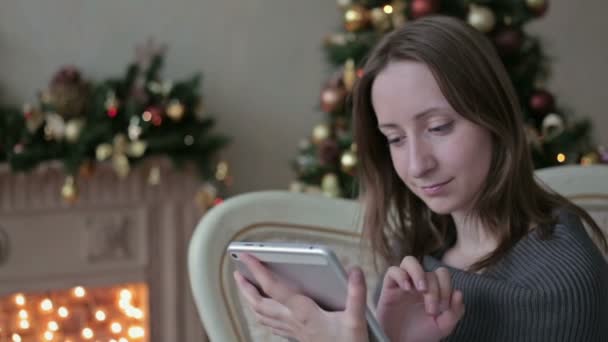 Happy woman looking in tablet PC in front of Christmas tree - Metraje, vídeo