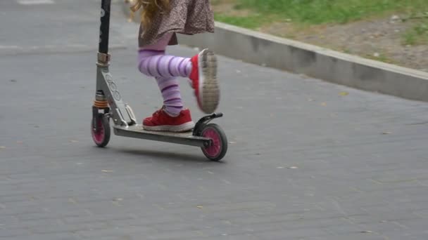 Little Blonde Girl Red Sneakers Close Up Tilt Up Girl is Riding The Kick Scooter Upward by Hill Sity Street Road Sign Parking Parked Cars Slow Motion - Záběry, video