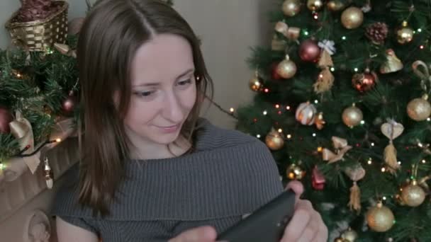 Žena pomocí svého mobilního telefonu na Vánoce doma v obývacím pokoji - Záběry, video