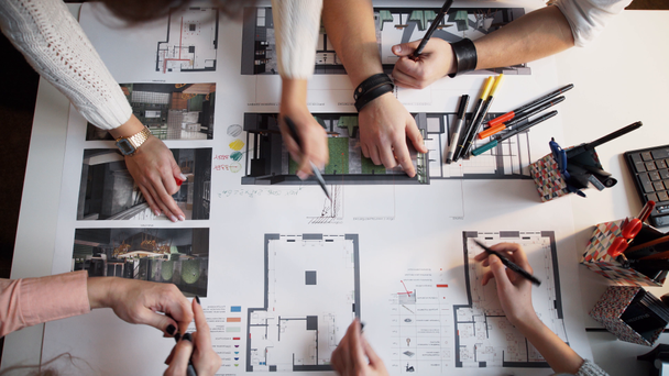 Primer plano de cuatro arquitectos discutiendo el plan juntos en el escritorio con planos
 - Metraje, vídeo