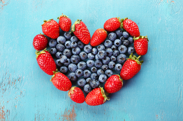Heart shaped strawberries and blueberries on blue wooden background - Fotoğraf, Görsel