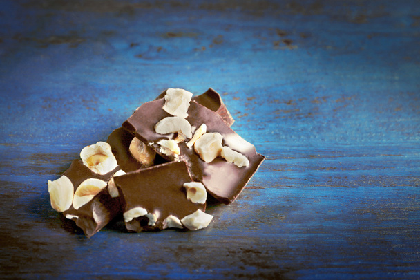 Black chocolate pieces with nuts on color wooden background - Φωτογραφία, εικόνα