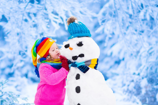 Küçük kız bir kar adam kışın bina - Fotoğraf, Görsel