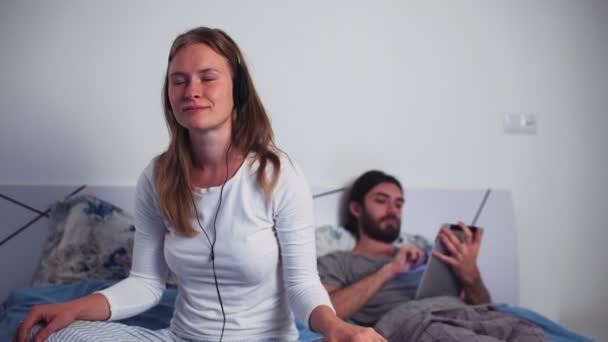 Frau hört Musik über Kopfhörer und Mann mit Tablet im Bett - Filmmaterial, Video