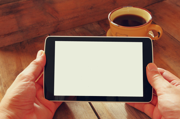 Digital tablet computer with isolated screen in male hands over wooden table background and cup of coffee. - Photo, Image