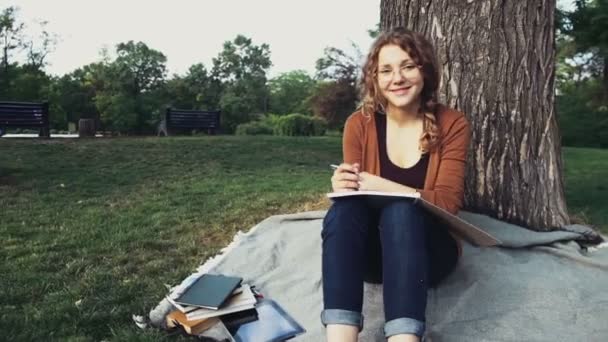 公園の木の下で座っている笑顔の女子学生の肖像画 - 映像、動画