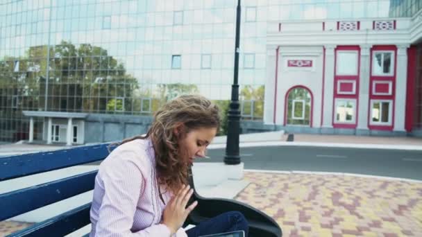 студентка сидит на скамейке с планшетом рядом с современным зданием
 - Кадры, видео