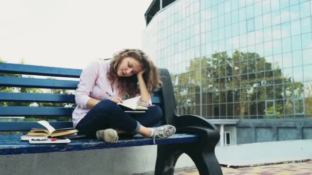 studentka sedí na lavičce poblíž moderní budova Zpomalený pohyb - Záběry, video