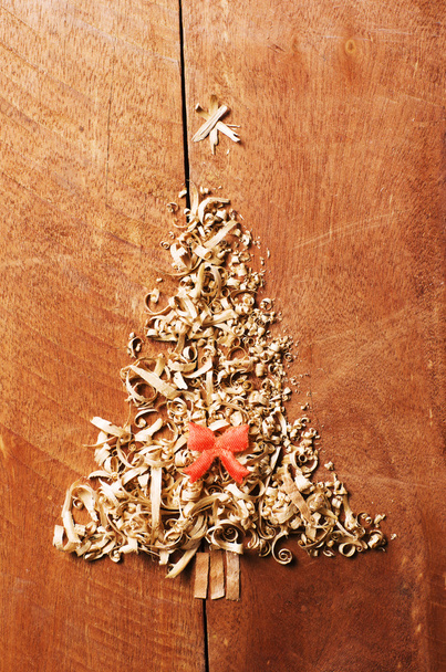 Simple Christmas tree arranged from sawdust, wood-chips on wooden background. Orange cute ribbon. - Photo, Image