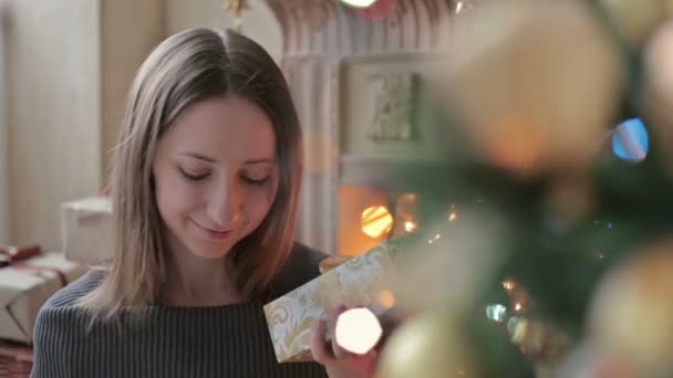 Young woman with gifts in front of Christmas tree - Footage, Video
