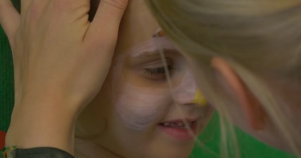 Educatrice Giovane Bionda sta dipingendo il volto di una bambina Bionda Dipingere il muso del gatto sul viso della ragazza con il pennello in aula dell'asilo
 - Filmati, video