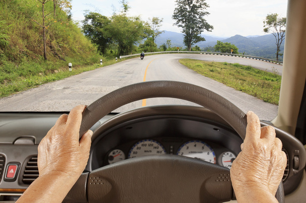 Ανώτερος γυναίκα οδήγηση ενός αυτοκινήτου στο δρόμο του βουνού. - Φωτογραφία, εικόνα