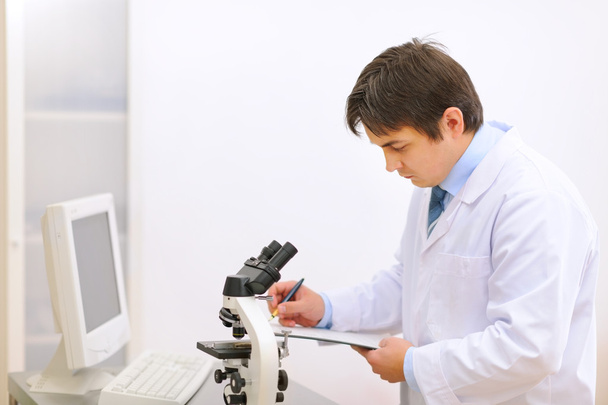 Researcher using microscope in medical laboratory and taking not - Photo, Image