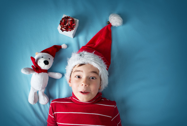 Happy boy in santa claus hat with a white bear on blue background - Фото, зображення