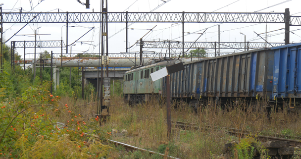 Green Electric Freight Locomotive tira del tren de carga largo Gris y azul vagones de carga Soportes del puente de la red de contacto del ferrocarril a través del ferrocarril
 - Metraje, vídeo