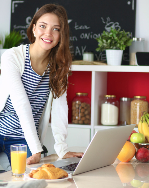 Attractive young woman using laptop and sitting in the kitchen - Photo, Image