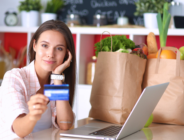 Smiling woman online shopping using tablet and credit card in kitchen - Foto, Imagen