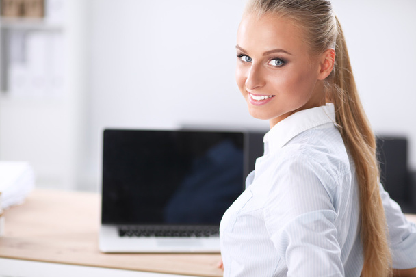 Attractive businesswoman sitting on a desk with laptop in the office - Foto, Imagem