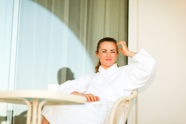 Young woman in bathrobe sitting at table on terrace and thinking - Fotoğraf, Görsel
