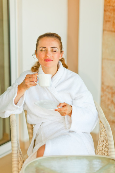 Young woman in bathrobe enjoying cup of coffee on terrace - Foto, Imagen