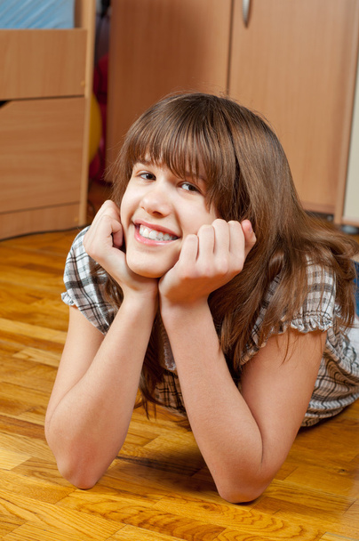 süßes lächelndes Teenie-Mädchen liegt auf dem Holzboden ihres Zimmers - Foto, Bild