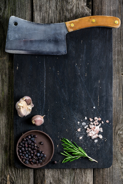 Cutting board, meat cleaver and condiments on dark wooden background - 写真・画像