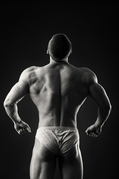 Professionele bodybuilder toont zijn lichaam op een donkere achtergrond - Foto, afbeelding