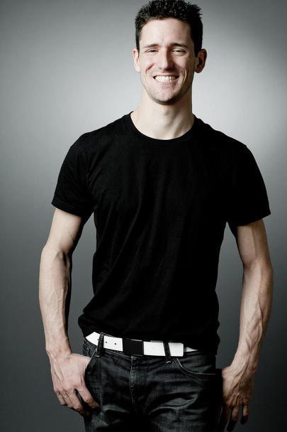 Jonge man in zwart t-shirt op grijze achtergrond.  - Foto, afbeelding