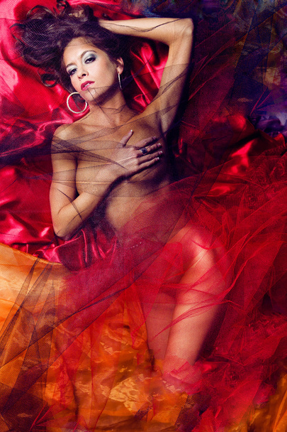 Beautiful lady laying down on red fabric. - Фото, изображение