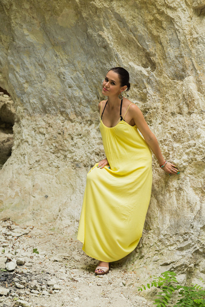 schöne Brünette in einem gelben Kleid auf einem Hintergrund aus Stein - Foto, Bild
