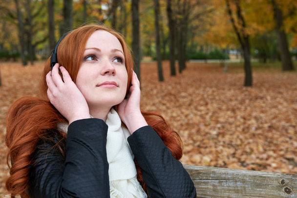 pelirroja escuchar música en el parque de la ciudad, temporada de otoño
 - Foto, imagen