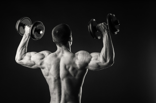 Musclé homme prend des exercices avec haltères sur un fond sombre
 - Photo, image