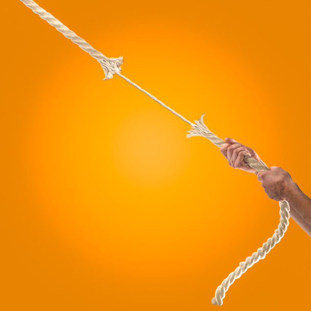 オレンジ色の背景に、ロープを引っ張る人の手。競争の概念 - 写真・画像