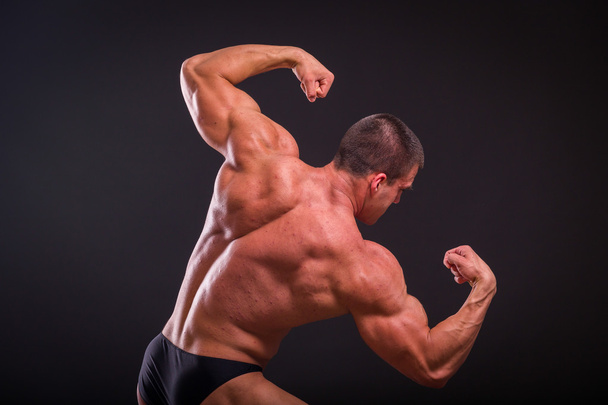 Professional bodybuilder shows his body on a dark background - Фото, изображение