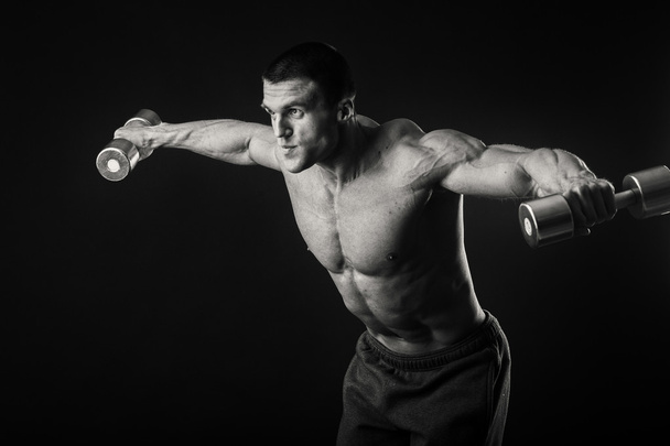 Мускулистый человек делает упражнения с гантелями на темном фоне
 - Фото, изображение