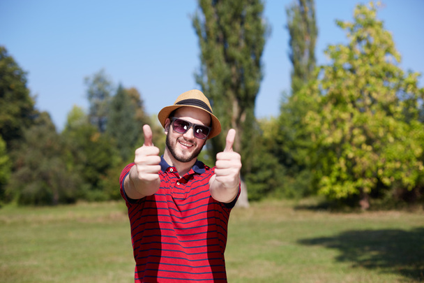 Young Casual Man Showing Thumbs Up And Smiling In The Park - Valokuva, kuva