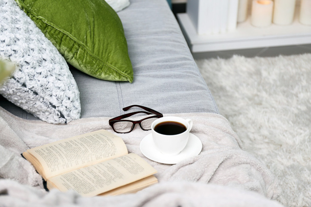 Cup of coffee with book on sofa in room - Foto, Imagem
