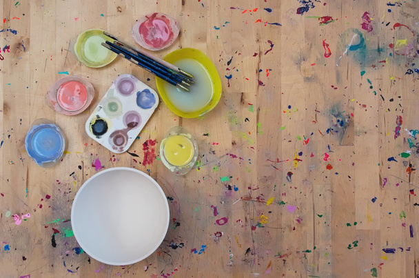 Aquarel verf, penselen en een witte kom op licht gekleurd - Foto, afbeelding