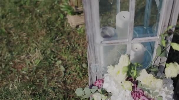 Bruiloft decoratie van huwelijksceremonie buitenshuis. Witte kaarsen en bloemen in de tuin. Close-up. Pan schot - Video