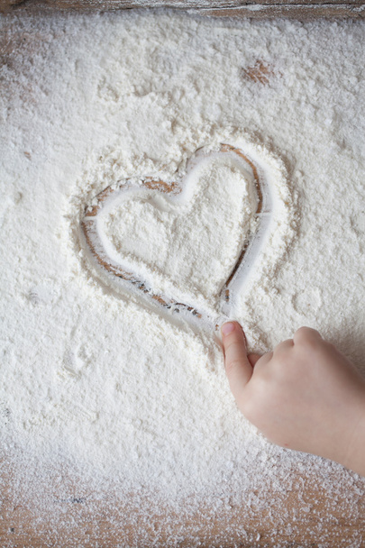 Corazón de harina sobre un escritorio de madera pintado por un niño
 - Foto, imagen