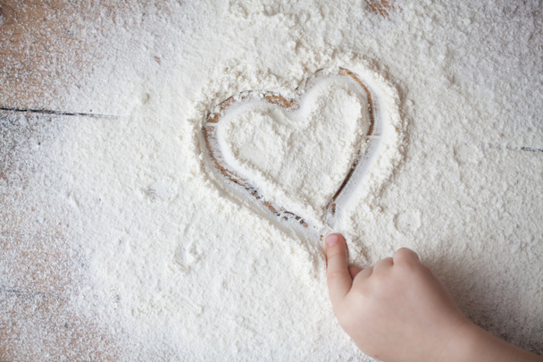 Corazón de harina sobre un escritorio de madera pintado por un niño
 - Foto, imagen