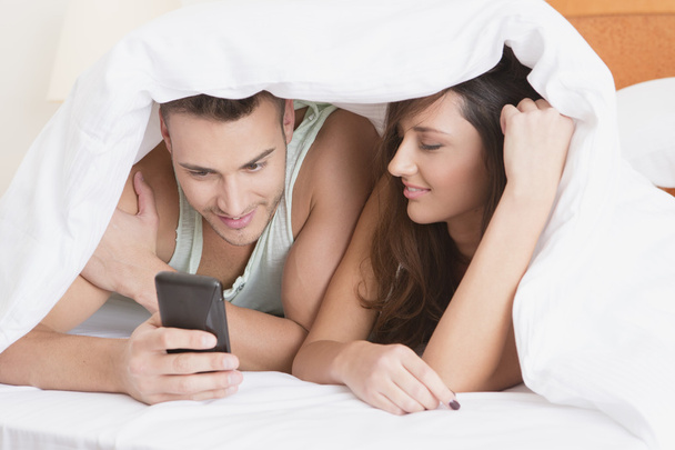 Happy couple under the covers looking at phone - Foto, imagen