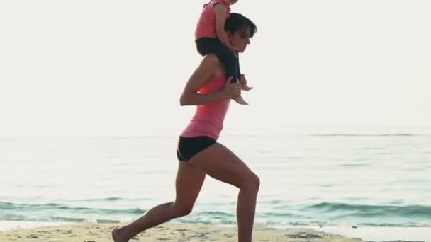 мати з дитиною на плечах робить присідання на пляжі повільним рухом
 - Кадри, відео