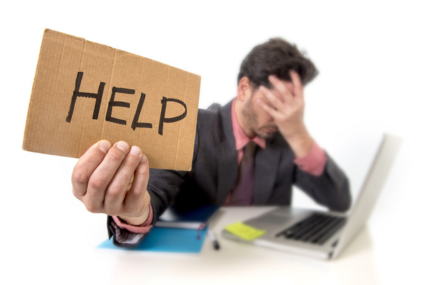 Homme d'affaires en costume et cravate assis au bureau de travail sur ordinateur portable demandant de l'aide tenant signe de carton
 - Photo, image