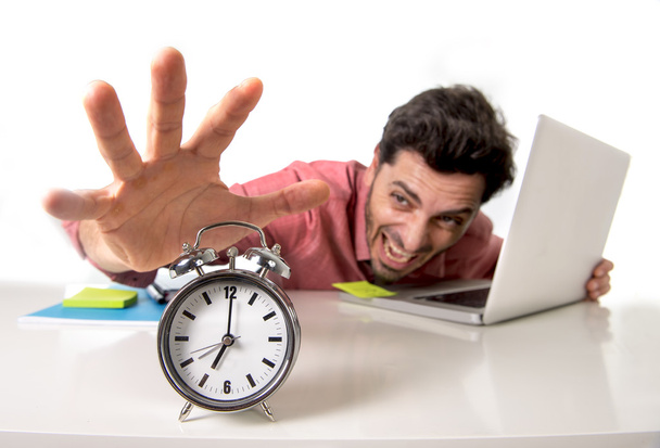 crazy businessman switching off alarm clock sitting at office desk working with computer laptop in deadline project concept - 写真・画像