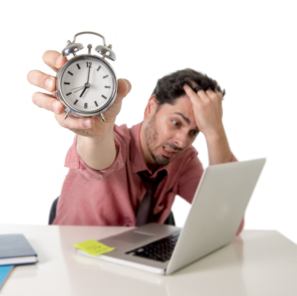 depressed businessman holding alarm clock sitting at office desk working with computer laptop in deadline project concept - 写真・画像