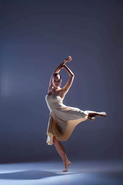 Young beautiful dancer in beige dress dancing on gray background - Foto, imagen
