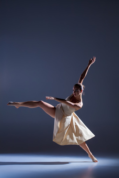 Young beautiful dancer in beige dress dancing on gray background - Фото, зображення
